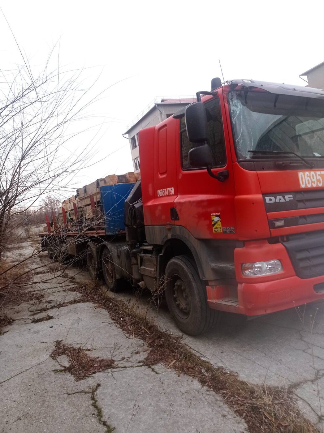 Cap tractor DAF roșu cu macara lângă hală