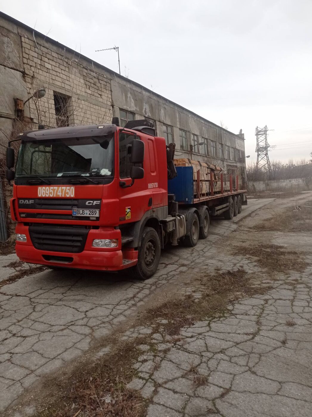 Camion roșu DAF cu manipulator lângă clădire industrială